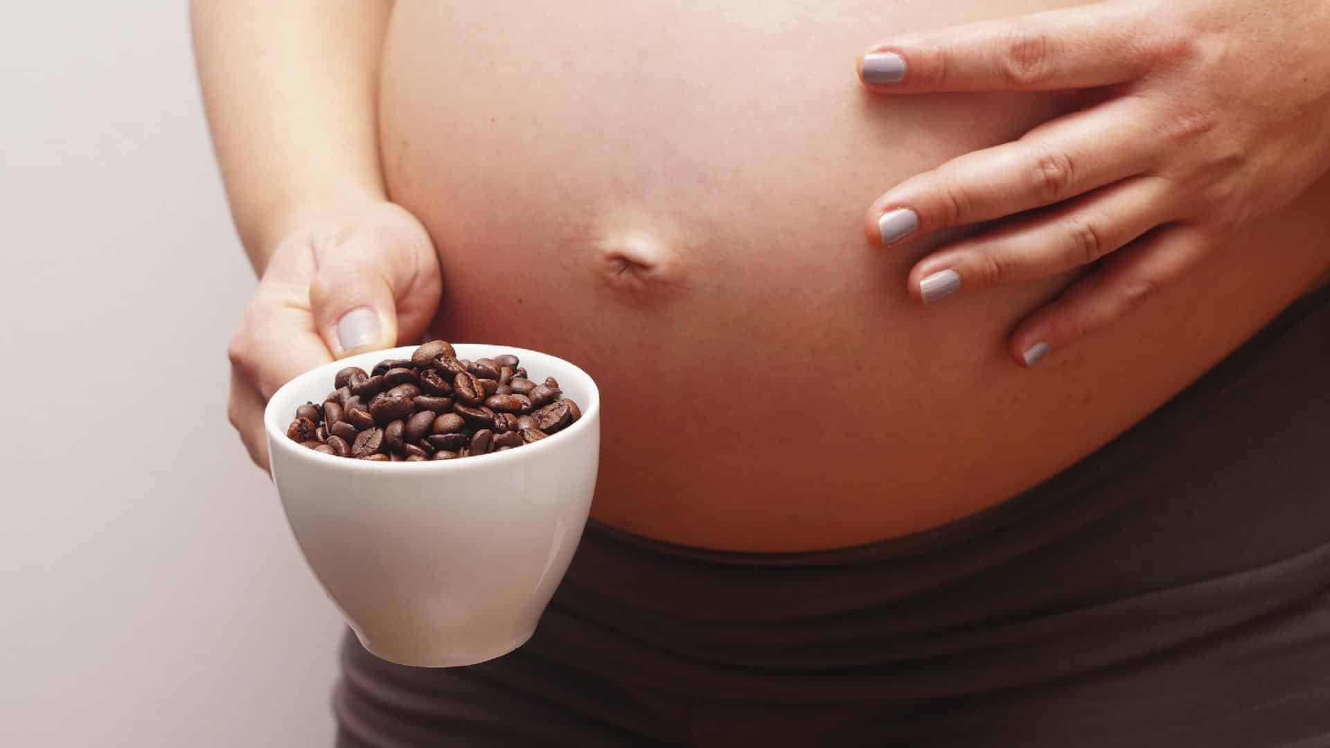 Mulher grávida segurando xícara com grãos de café visíveis