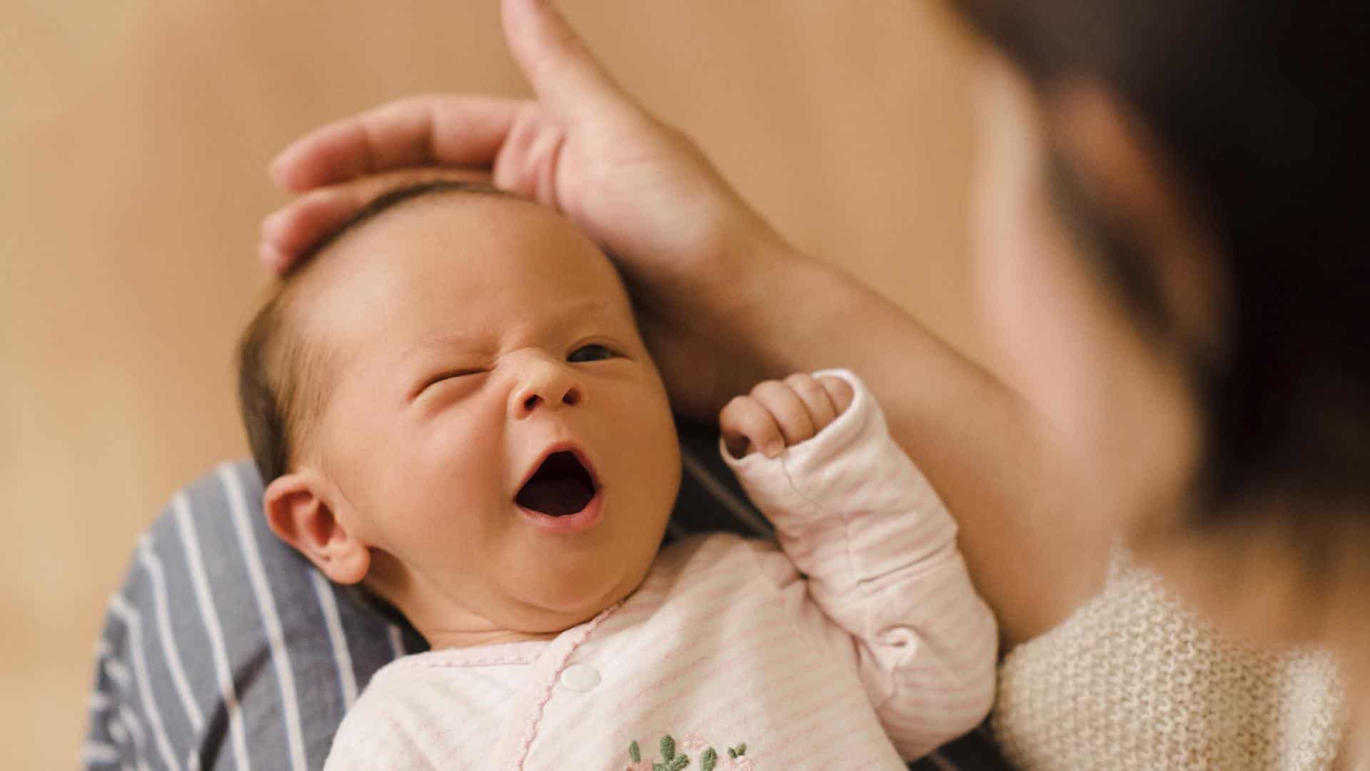 Bebê no colo de sua mãe com expressão fofa e sonolenta