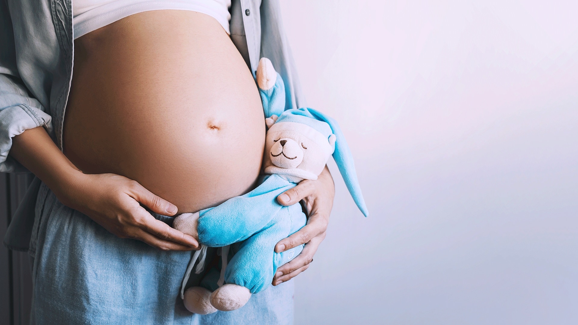 Mulher grávida segurando um ursinho perto de sua barriga